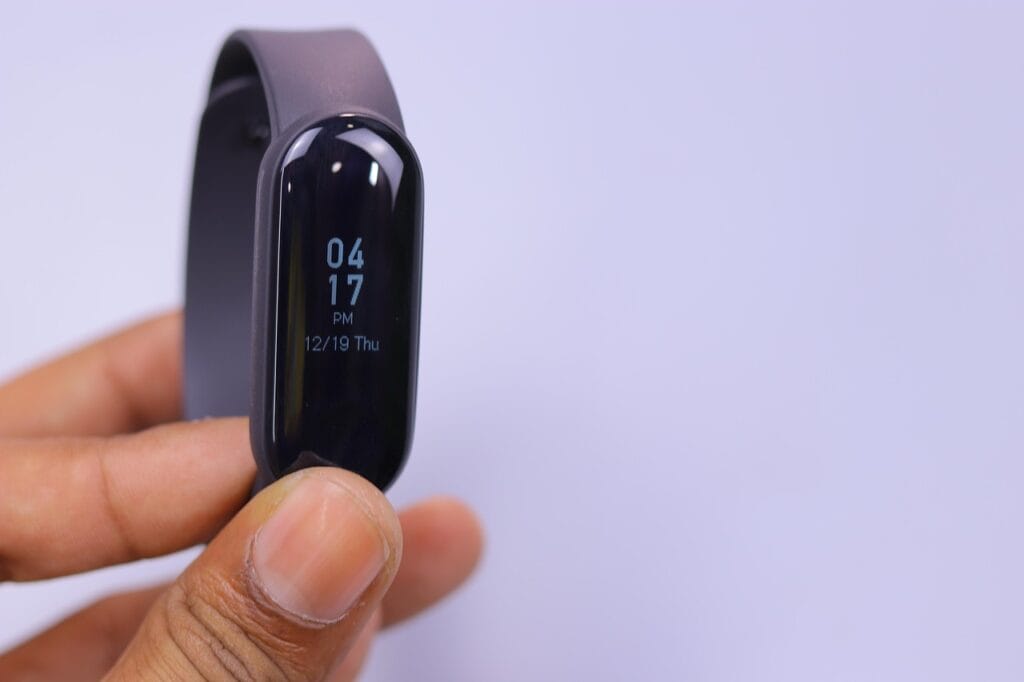 Hand holding a black fitness tracker showing the date and time on its digital screen. Cardio at home